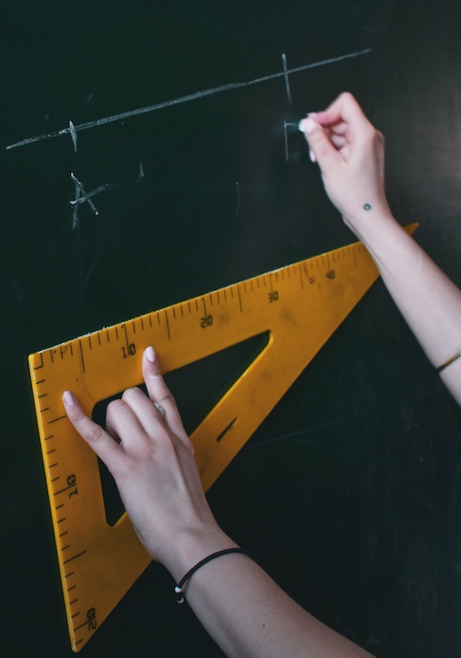 An online math tutor measuring with a triangular ruler while writing on the chalkboard.